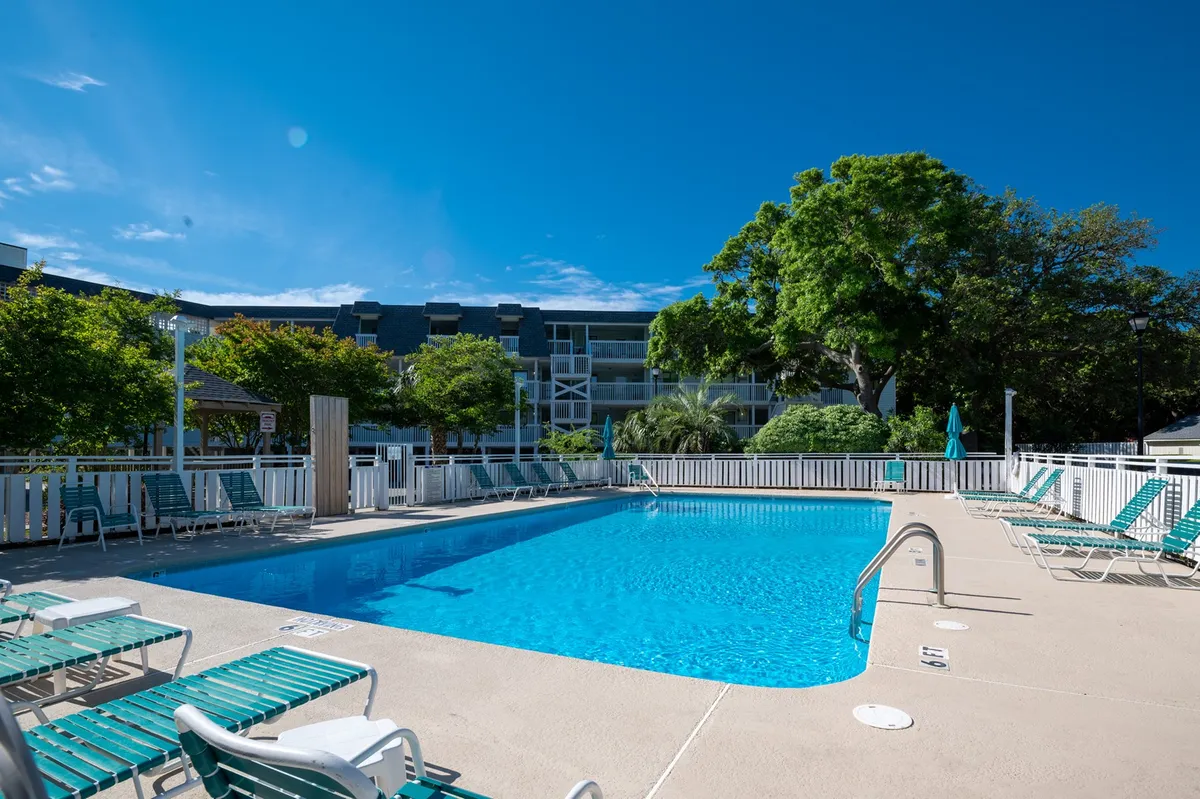 A sparkling outdoor swimming pool with inviting lounge chairs is surrounded by lush trees and the resort's building facade. The atmosphere is relaxed, with hints of social gatherings and quiet moments, making it ideal for families to unwind or play after the beach.