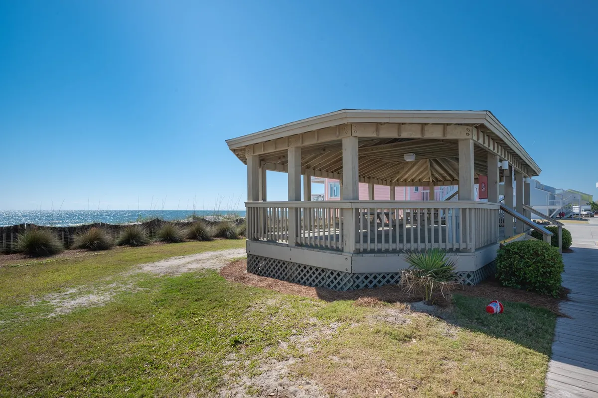 A cheerful outdoor scene featuring a gazebo with seating, ocean views, and surrounding greenery. The setting invites group gatherings, picnics, or simply enjoying the sea breeze together.