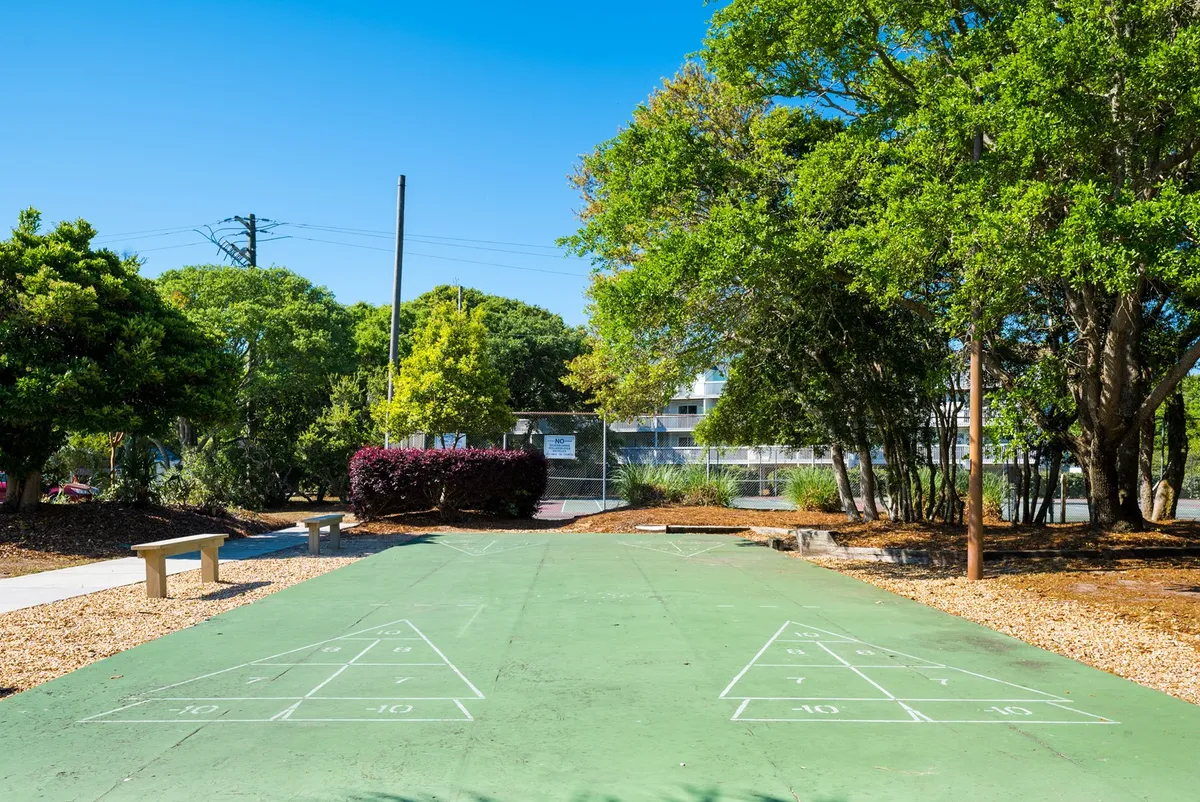 An exterior shuffleboard court bordered by greenery and a seating area, offering a playful and communal setting for outdoor leisure and friendly competition.