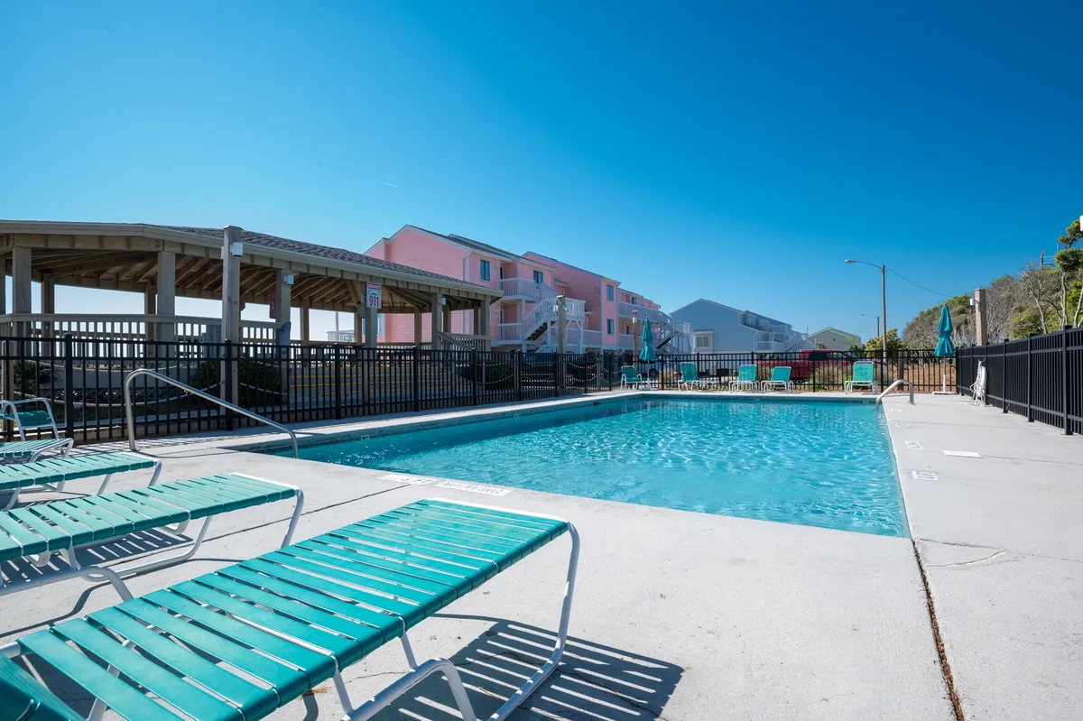 An exterior shot of a vibrant swimming pool area surrounded by lounge chairs and colorful resort buildings. The scene radiates leisure, fun, and the social aspects of the property’s amenities.