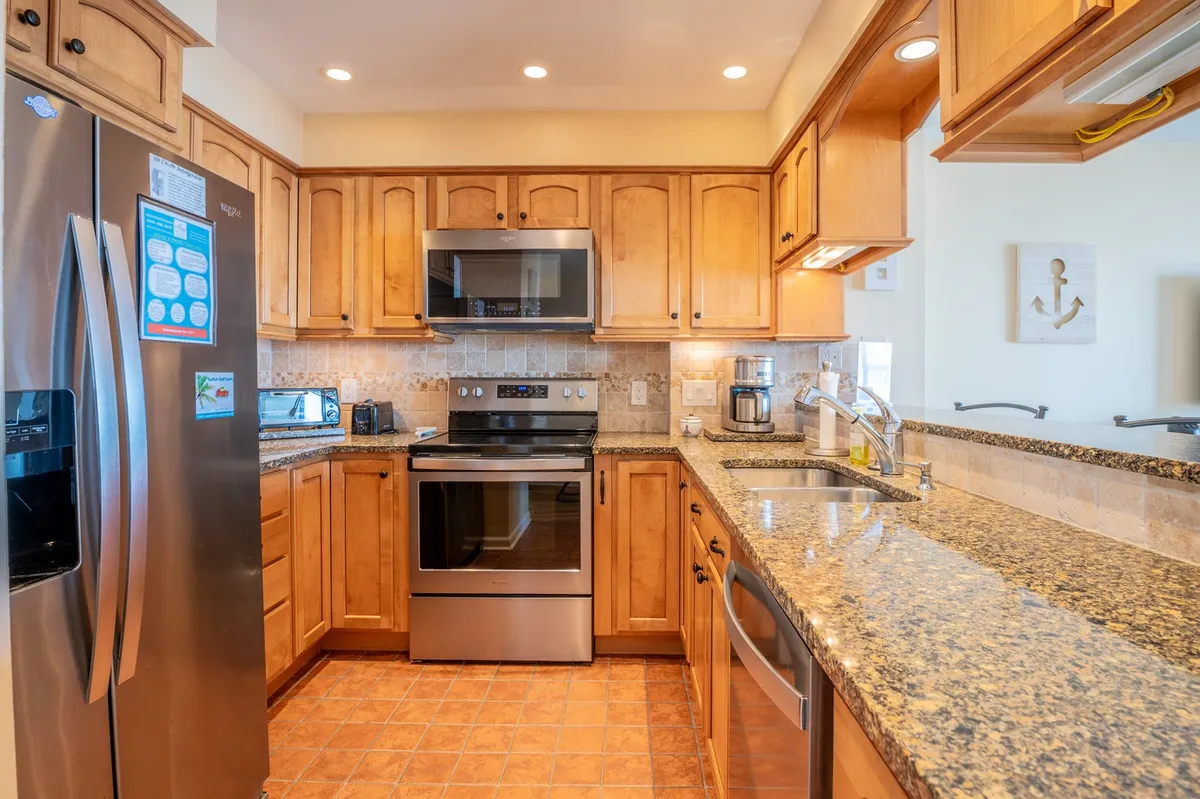 This image captures a stylish, upgraded kitchen with stainless steel appliances, granite countertops, and wood cabinetry. It's a warm, welcoming space designed for cooking, entertaining, and family gatherings. Ample counter space and inviting finishes make it ideal for both meal preparation and casual conversations.