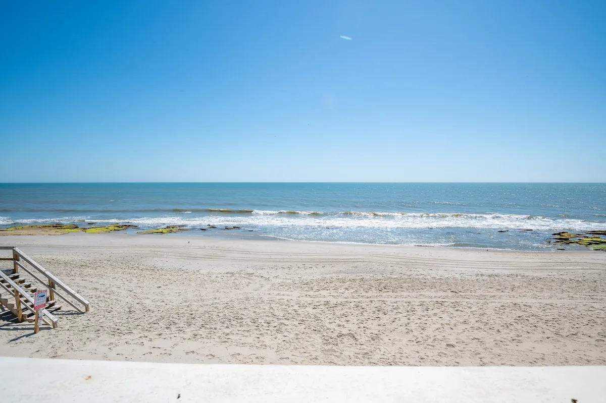 This image showcases a beautiful stretch of sandy beach meeting the ocean, with gentle waves and a tranquil sky overhead. The scene captures the direct beachfront access that Ocean Dunes 2003 offers, inviting families to step right onto the sand for sun, swimming, and beach adventures.