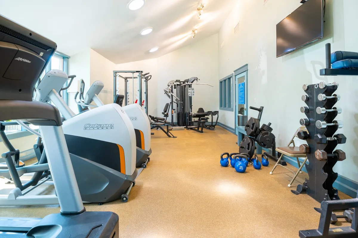 A modern, bright fitness center equipped with treadmills, weight machines, dumbbells, kettlebells, and large windows allowing in natural light. The space feels active and motivational, suited for guests looking to stay fit during their stay.