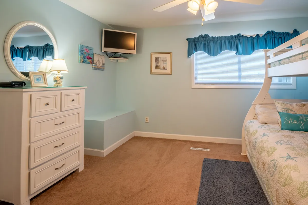 A playful and cheerful bunk room with a bunk bed, dresser, mirror, wall art, and a window bringing in natural light. The space is well-suited for children or extra guests, offering a relaxed setting for reading, playing, or sleepovers.