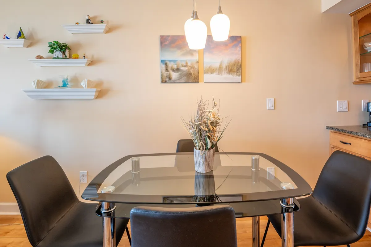 This scene features a glass dining table adorned with a floral centerpiece, illuminated by pendant lights and surrounded by comfortable seating. The background shows tasteful wall art, suggesting a space tailored for family dinners, celebrations, and social gatherings.
